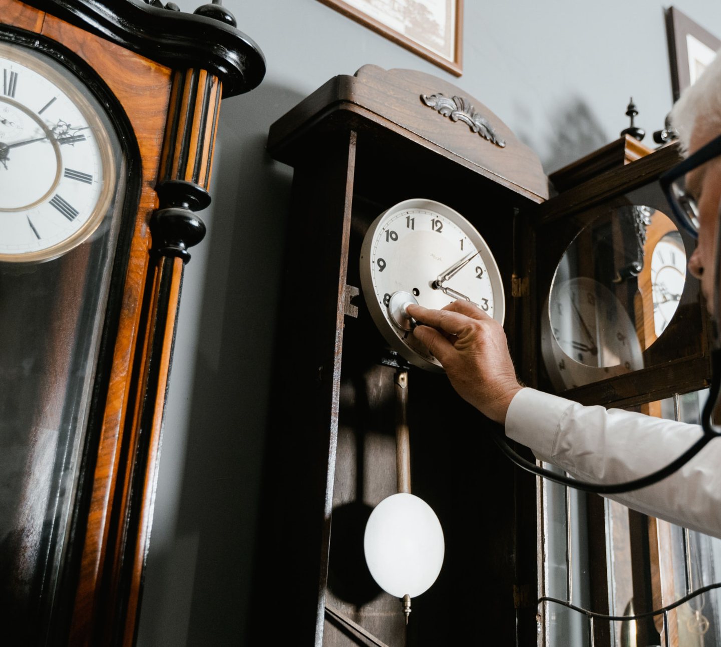 Un homme âgé règle le mécanisme d'une pendule ancienne, une horloge sur pied à sa gauche